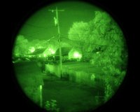 View through a green phosphor night vision goggle showing a nighttime scene with two people