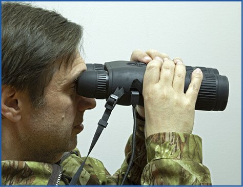 Hunter in camouflage jacket glassing at night through thermal binoculars in the field