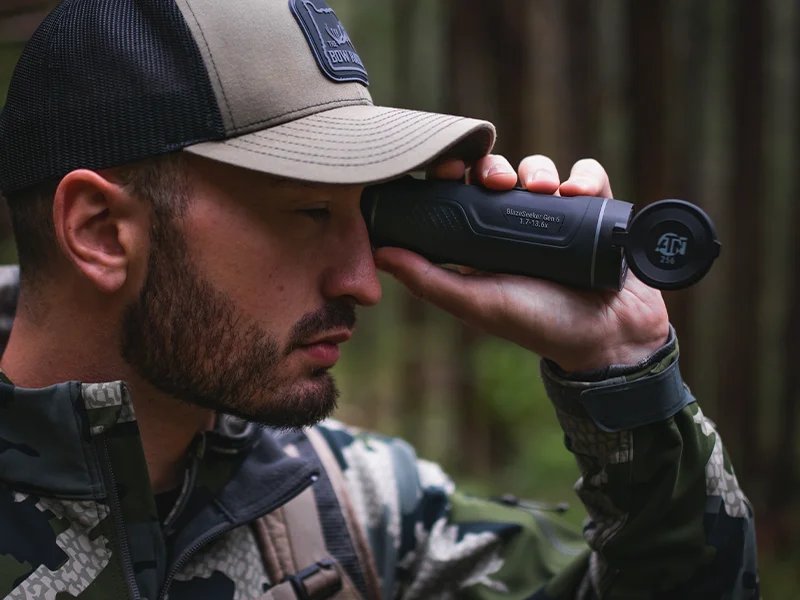 Man in camouflage clothing looking through the ATN BlazeSeeker 6 thermal monocular in a forest setting