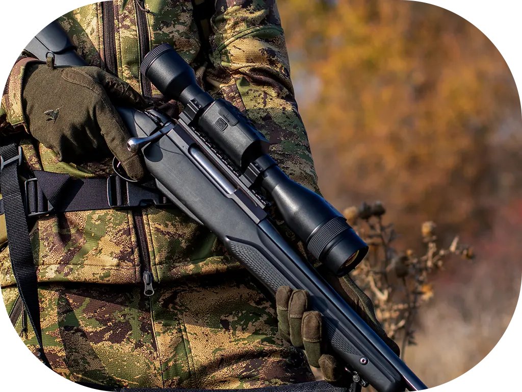 Close-up of a person in camouflage clothing and gloves holding a bolt-action rifle fitted with an ATN thermal scope